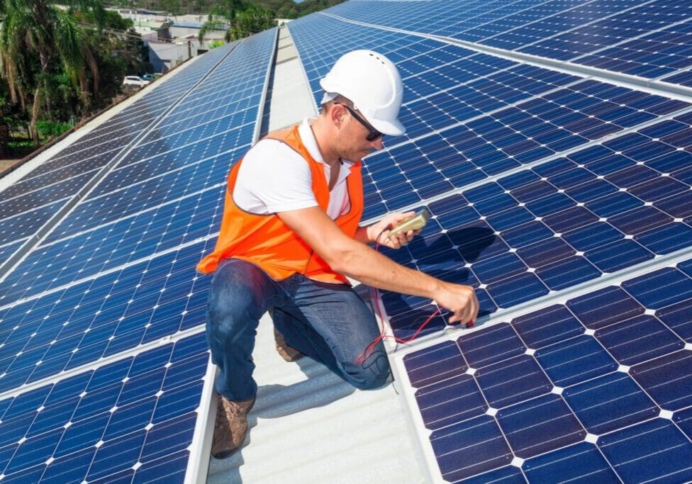 A man in an orange vest and hard hat working on solar panels.